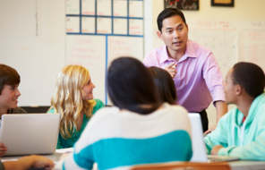 A male teacher of Asian descent instructs a group of students. 
