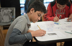 A student writes on a piece of paper in a classroom.