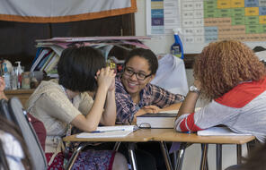 Three students in conversation while sitting at a desk.