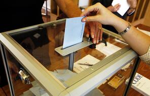 A voter places a ballot into a clear ballot box.