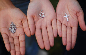Three hands holding the Hasma, the Star of David, and the Cross.