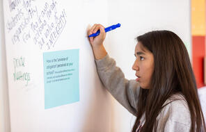 Student writes on poster board about the universe of obligation