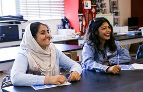 Two female students, one with a hijab, sit in classroom.