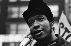 Black and white photo of Black Panther Party leader Fred Hampton speaking at a microphone 