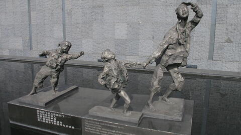 A statue featuring a woman running, holding hands with a young girl while another young girl trails behind them. All show expressions of fear and distress on their faces.
