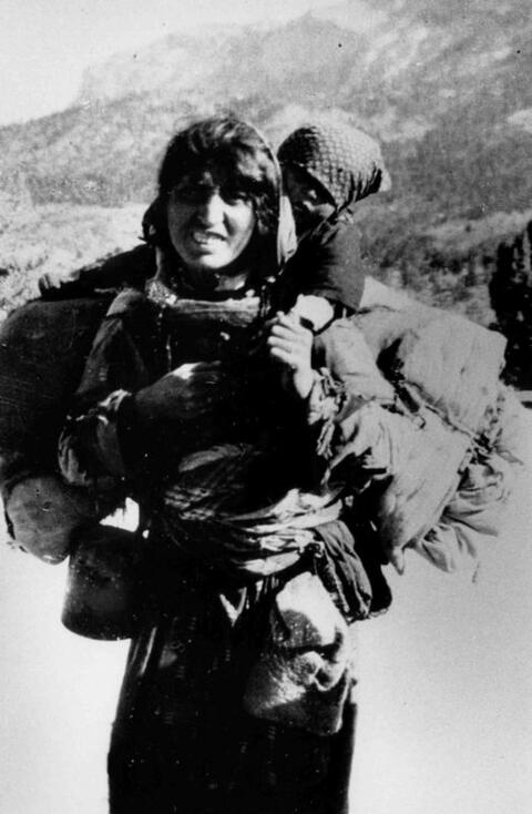 A black and white photo of an Armenian woman carrying her child on her back.