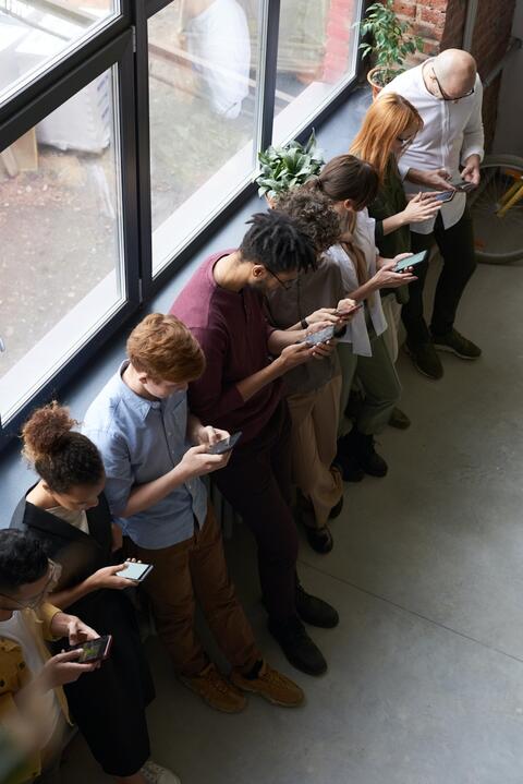 People standing in a line looking at their cellular phones.