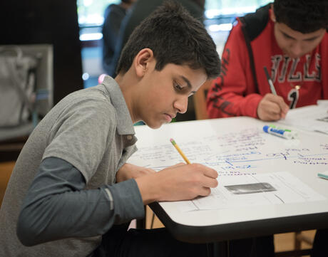 A student writes on a piece of paper in a classroom.