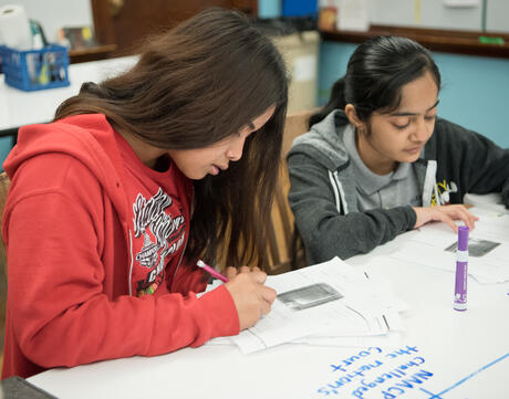 Two female students write at their desks. 