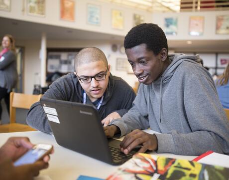 Two high school students look at a laptop screen in a school library