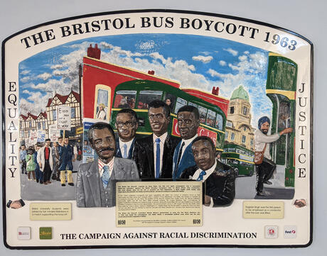 A commemorative plaque of the Bristol Bus Boycott showing a red building, a bus, and several people.