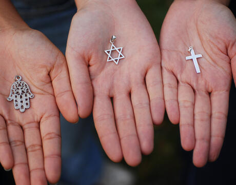 Three hands holding the Hasma, the Star of David, and the Cross.