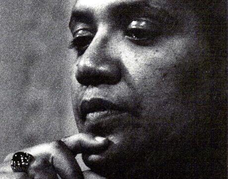 A headshot of Audre Lorde taken in 1980; her finger rests on her chin, and she is looking down