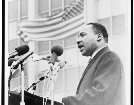 Martin Luther King, Jr., half-length portrait, facing left, speaking at microphones